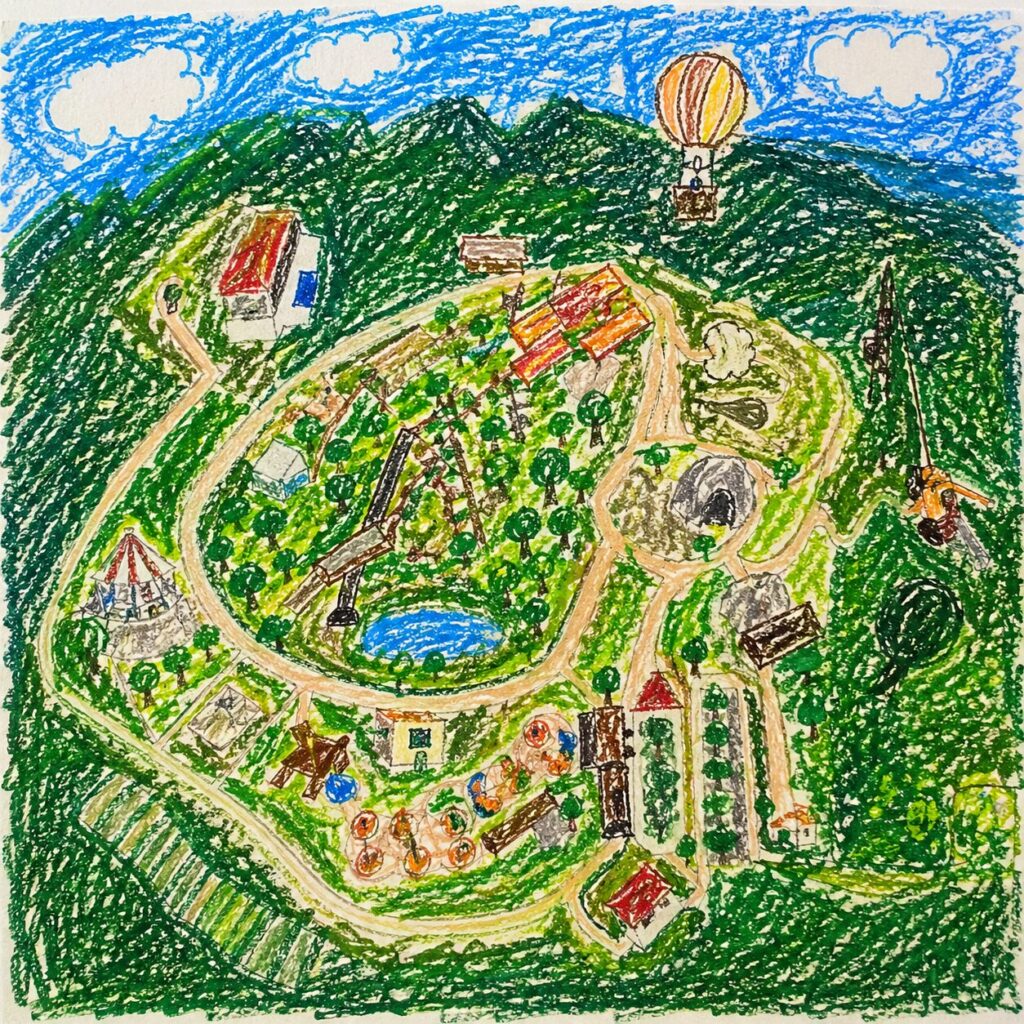 小学一年生の女の子がクレヨンで描いた、上空から見たジャングリア沖縄のイメージ図。緑の山々に囲まれた園内には、曲がりくねった道や建物、アトラクション、池などがカラフルに描かれている。空には青い空と白い雲、気球があり、全体的に元気で自由なタッチの絵。